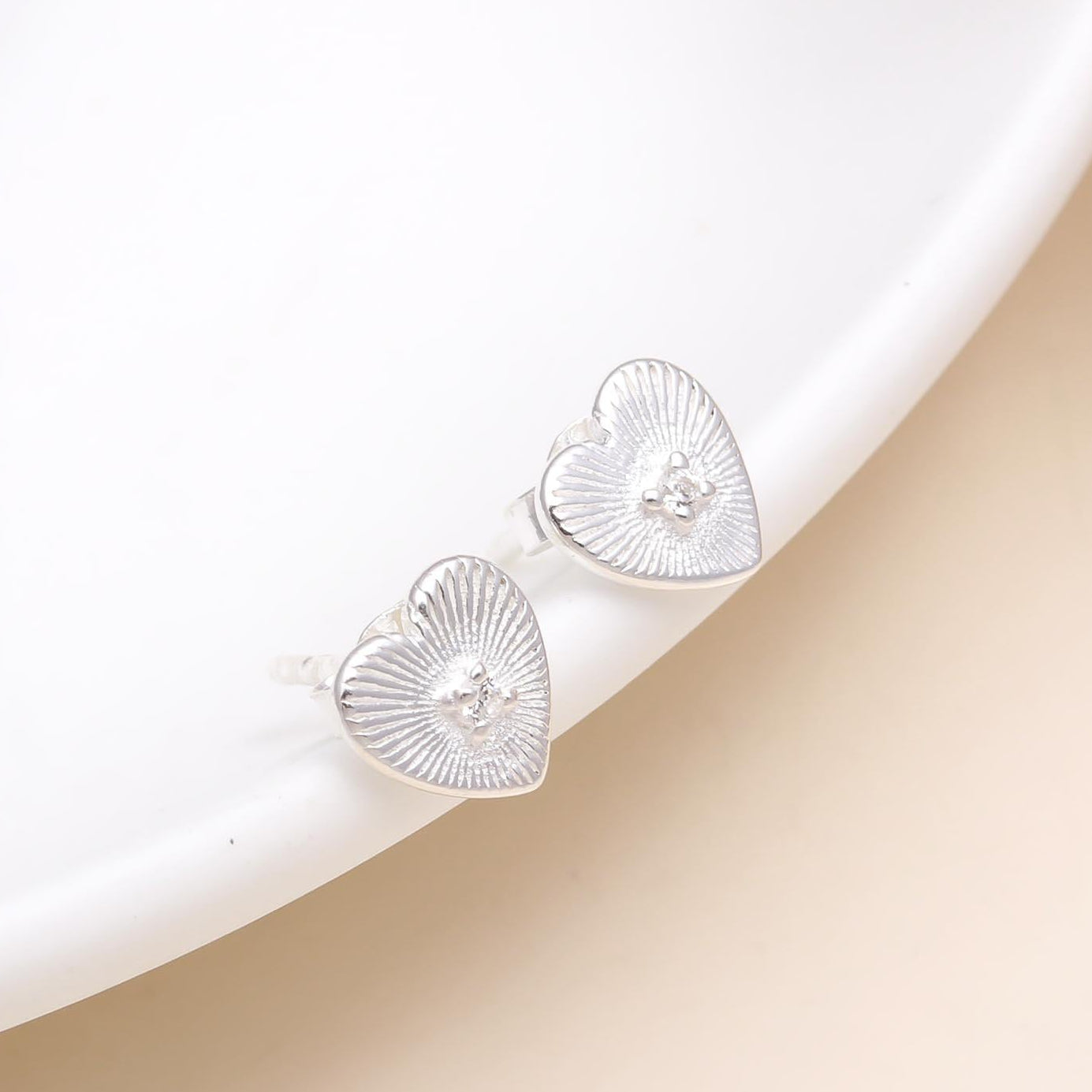 A pair of 925 sterling silver heart-shaped stud earrings placed on a white surface.