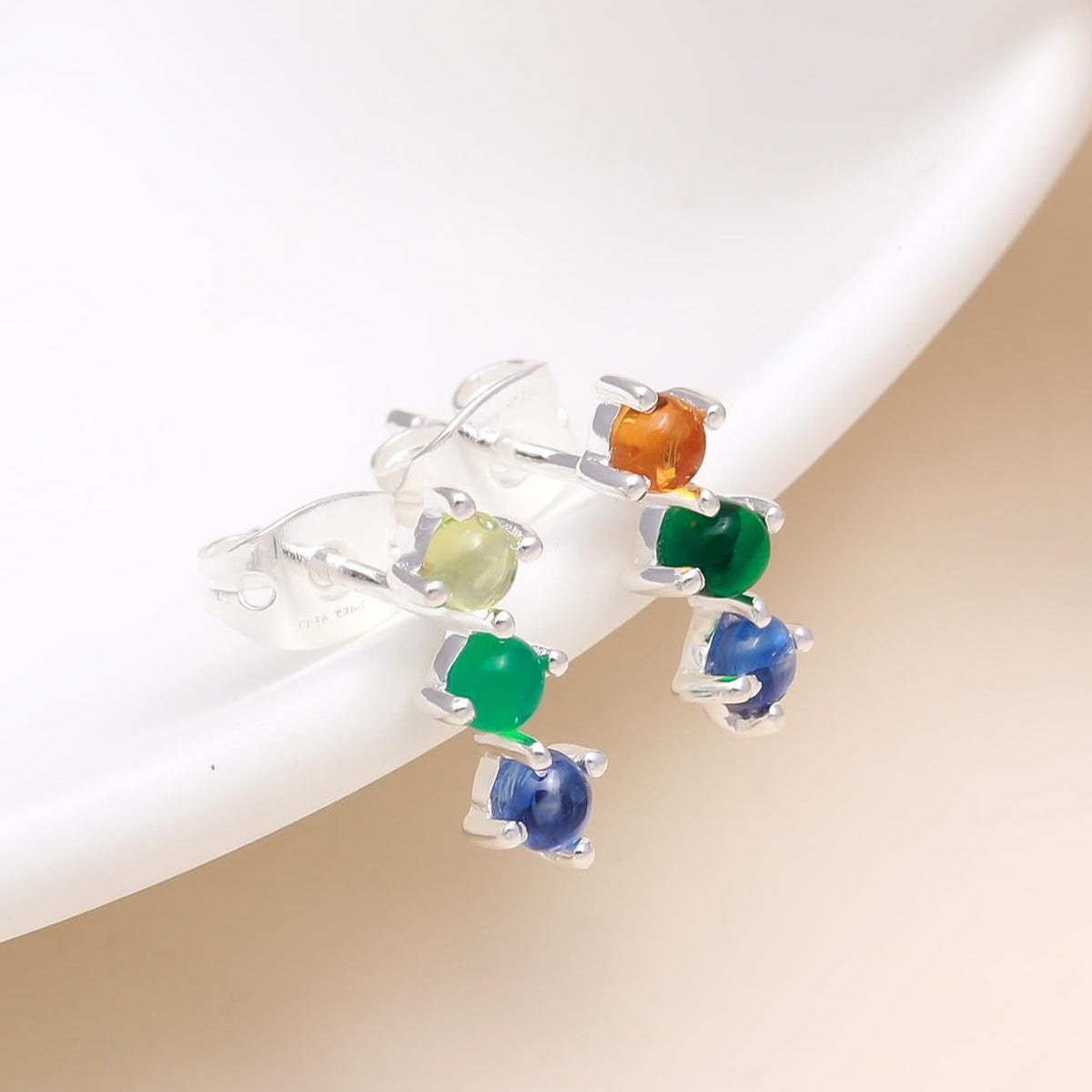 A pair of 925 sterling silver multicolor gemstone stud earrings displayed on a white surface, with the earrings showing a variety of colors including blue, green, and orange.