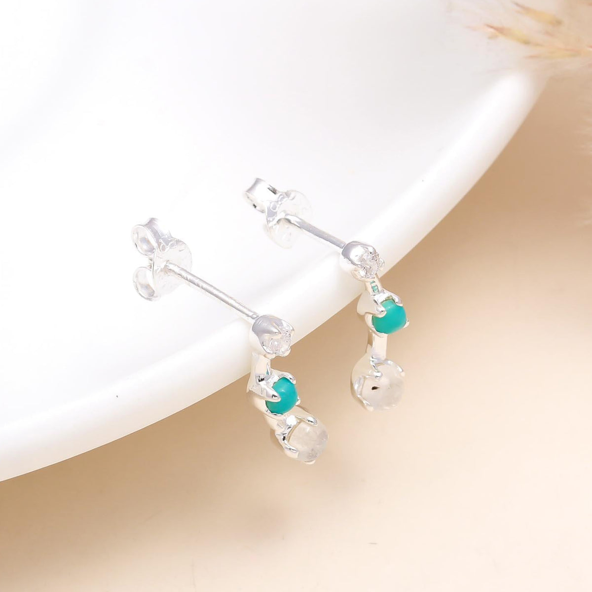 A pair of 925 sterling silver stud earrings with turquoise and clear quartz stones, displayed on a white surface.