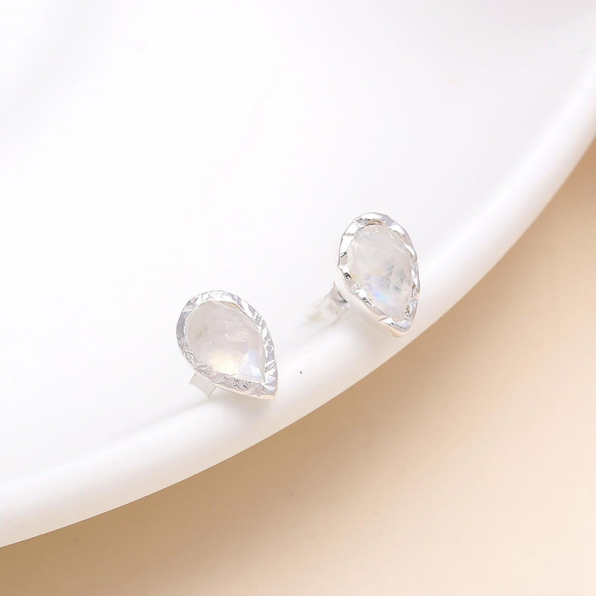 A pair of 925 sterling silver pear-cut moonstone stud earrings placed on a white surface.