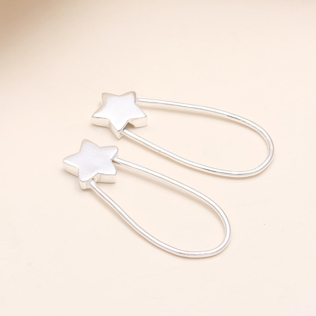 A pair of 925 sterling silver star drop earrings placed on a beige surface.