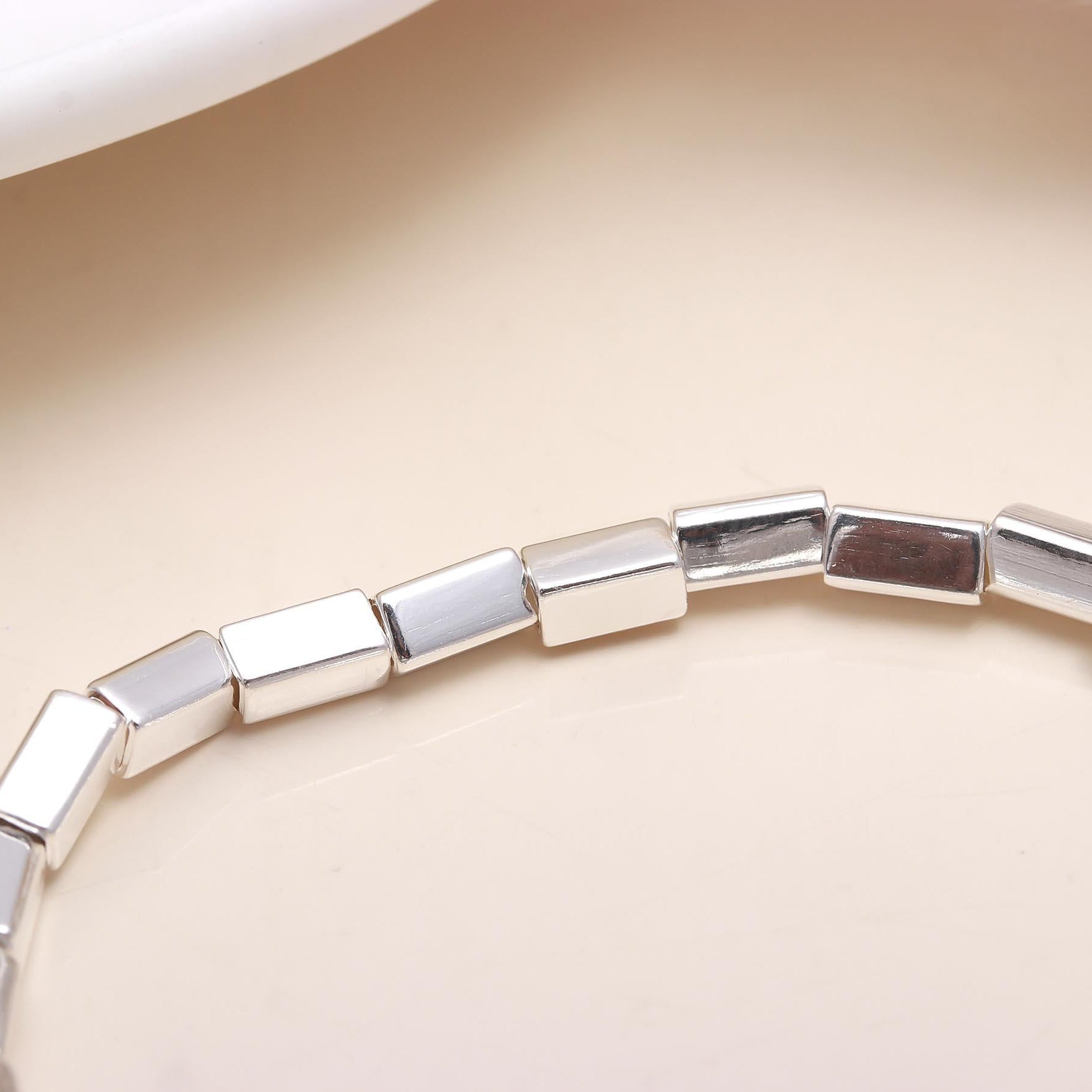 Silver bracelet with square beads on a beige background