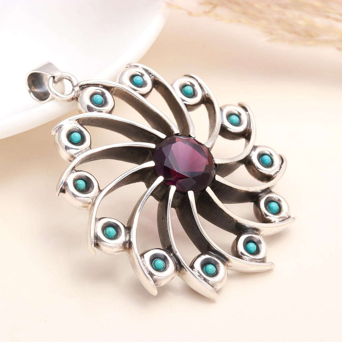 A vintage sterling silver pendant featuring a garnet at the center with turquoise accents arranged in a floral pattern around it.