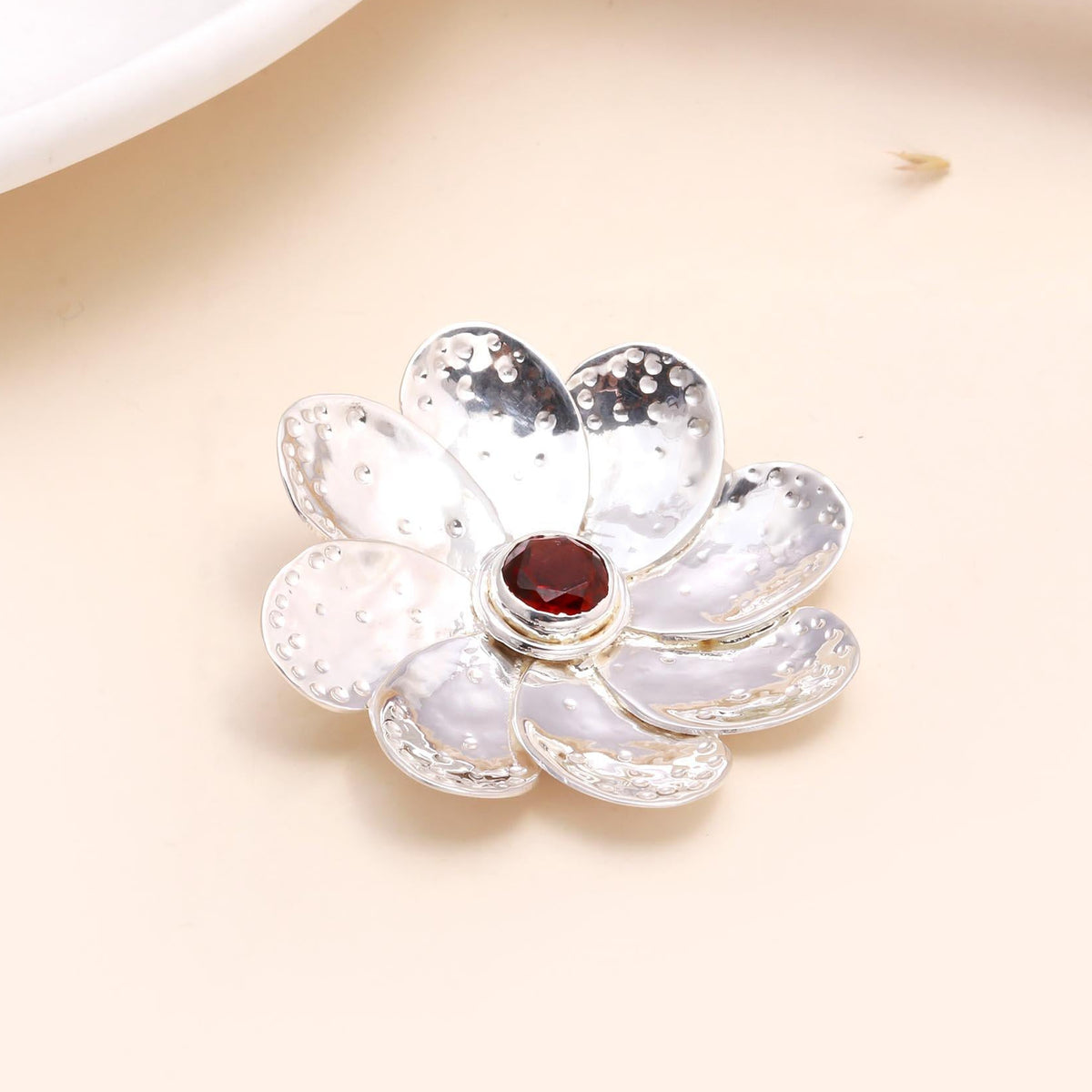 A 925 sterling silver pendant in the shape of a floral garnet flower with a deep-red gemstone at its center and intricate silverwork.