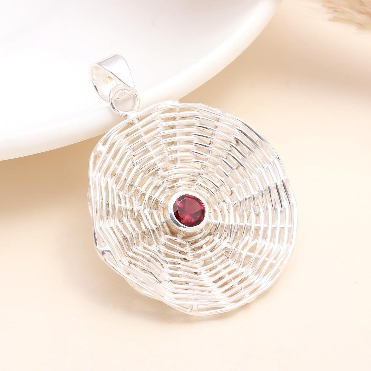 A 925 Sterling Silver Handwoven Garnet Pendant with a deep-red garnet gemstone at the center, placed on a white surface.