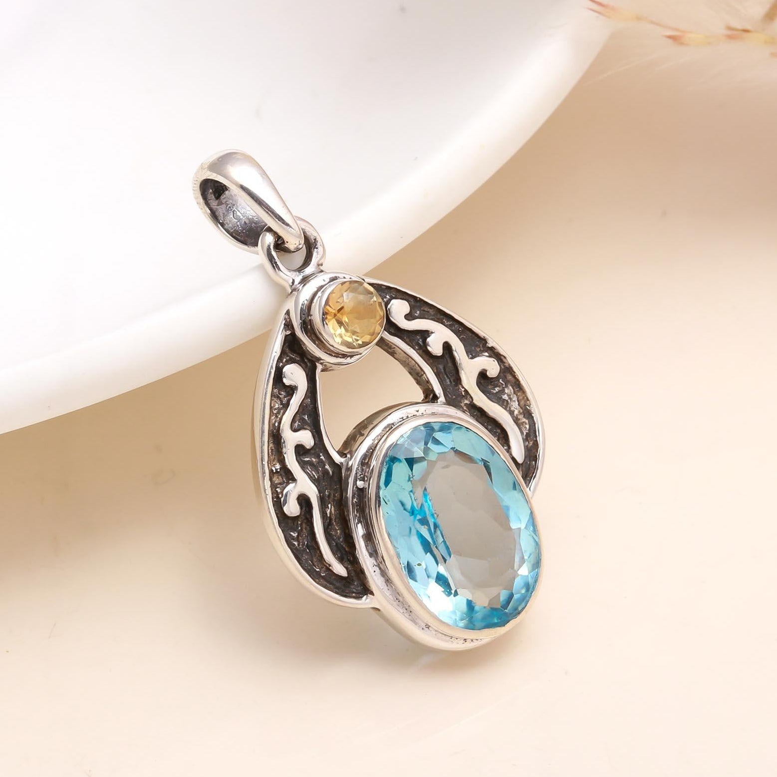 Silver pendant with blue gemstone and yellow stone on a beige background