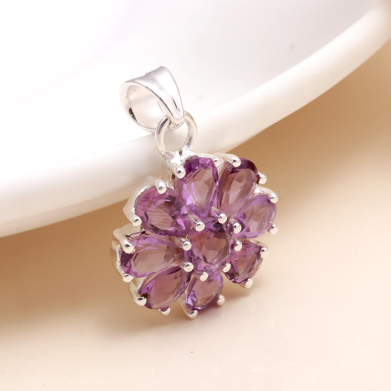 A 925 sterling silver pendant with a floral design, featuring natural amethyst gemstones in a purple color, displayed against a beige background.