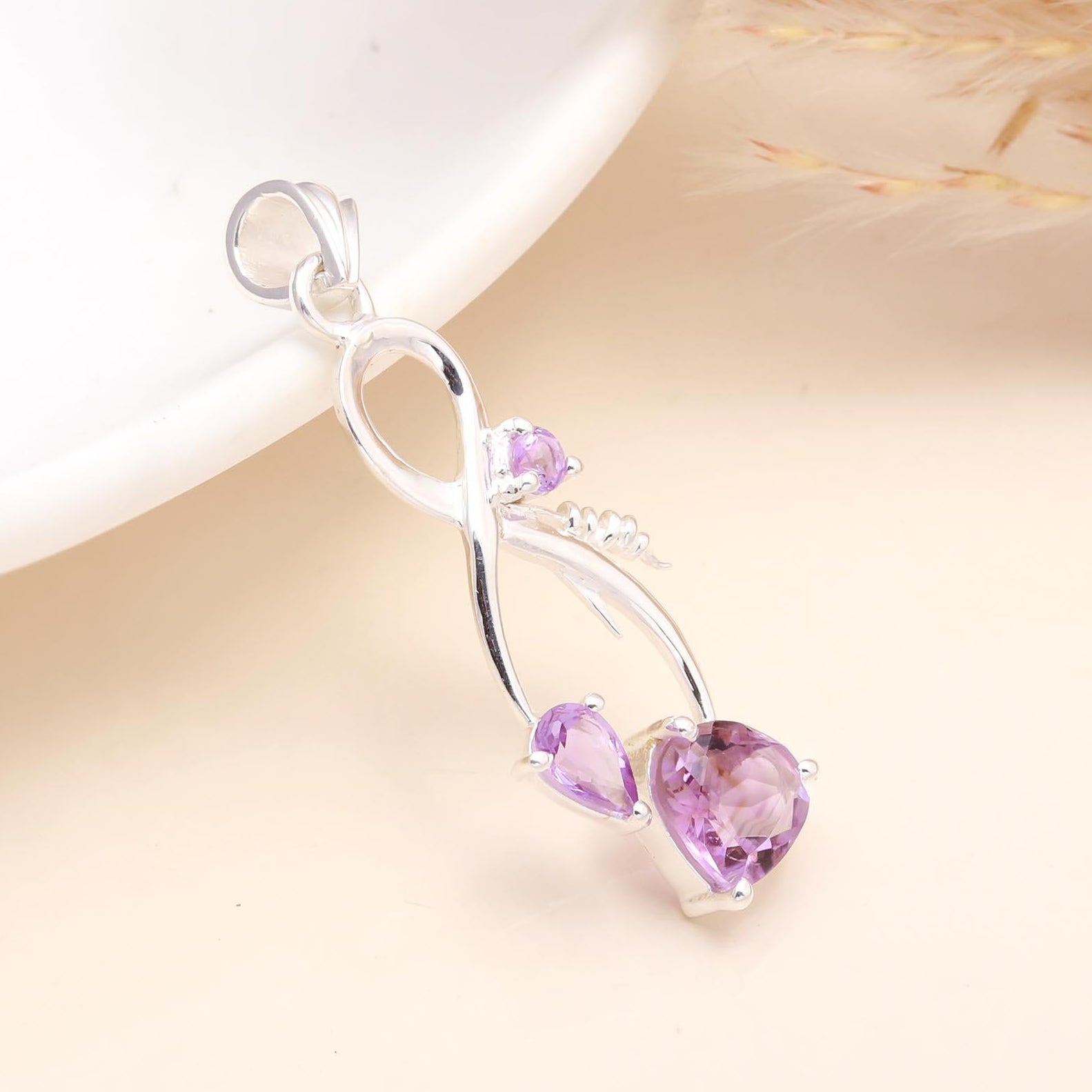 A 925 sterling silver infinity pendant featuring a natural amethyst gemstone, placed on a white surface.
