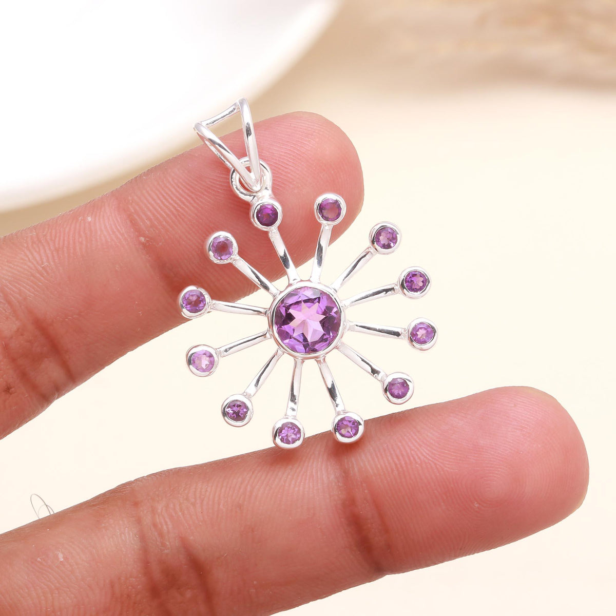 Silver pendant with purple gemstones held between fingers on a neutral background