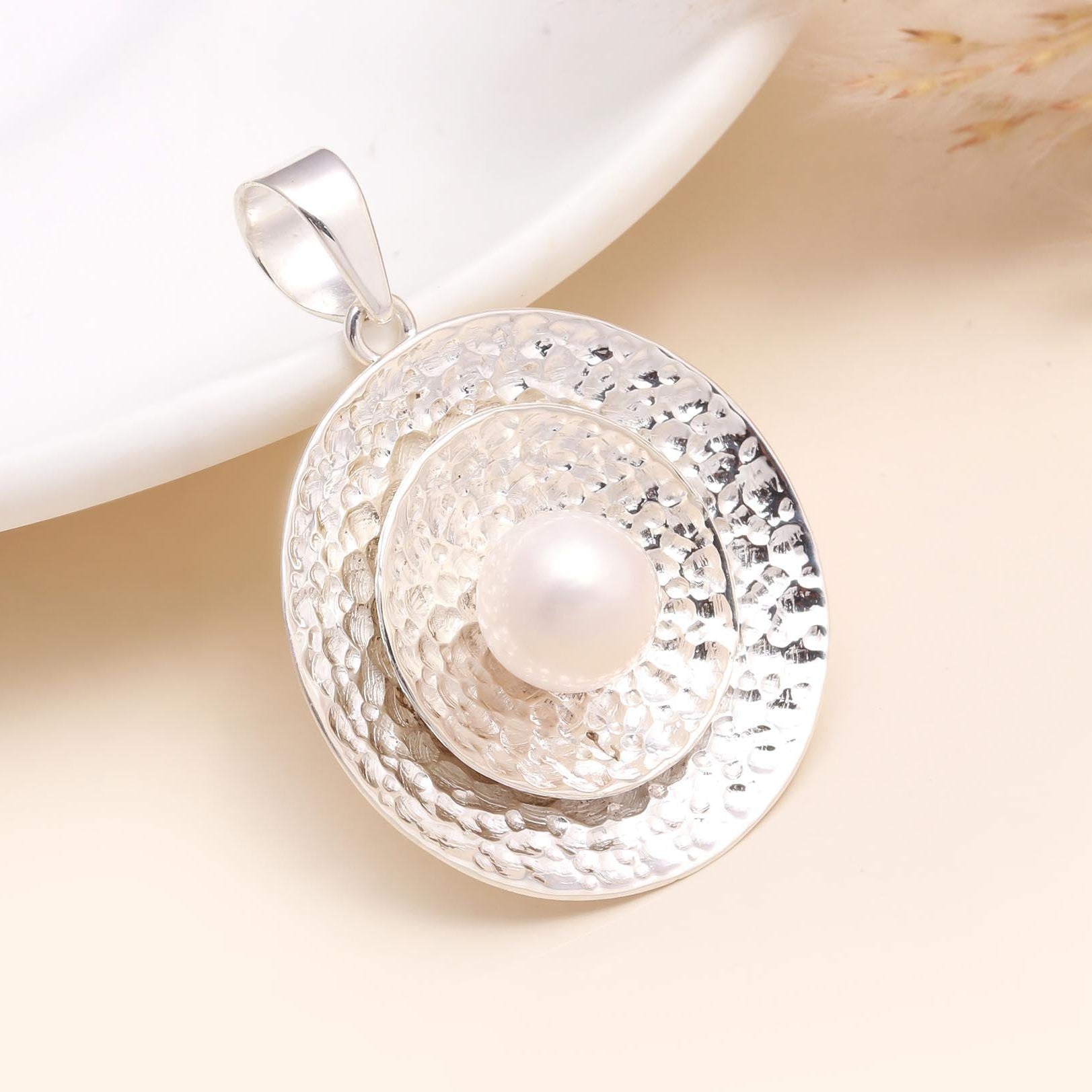 Silver pendant with a pearl on a beige background