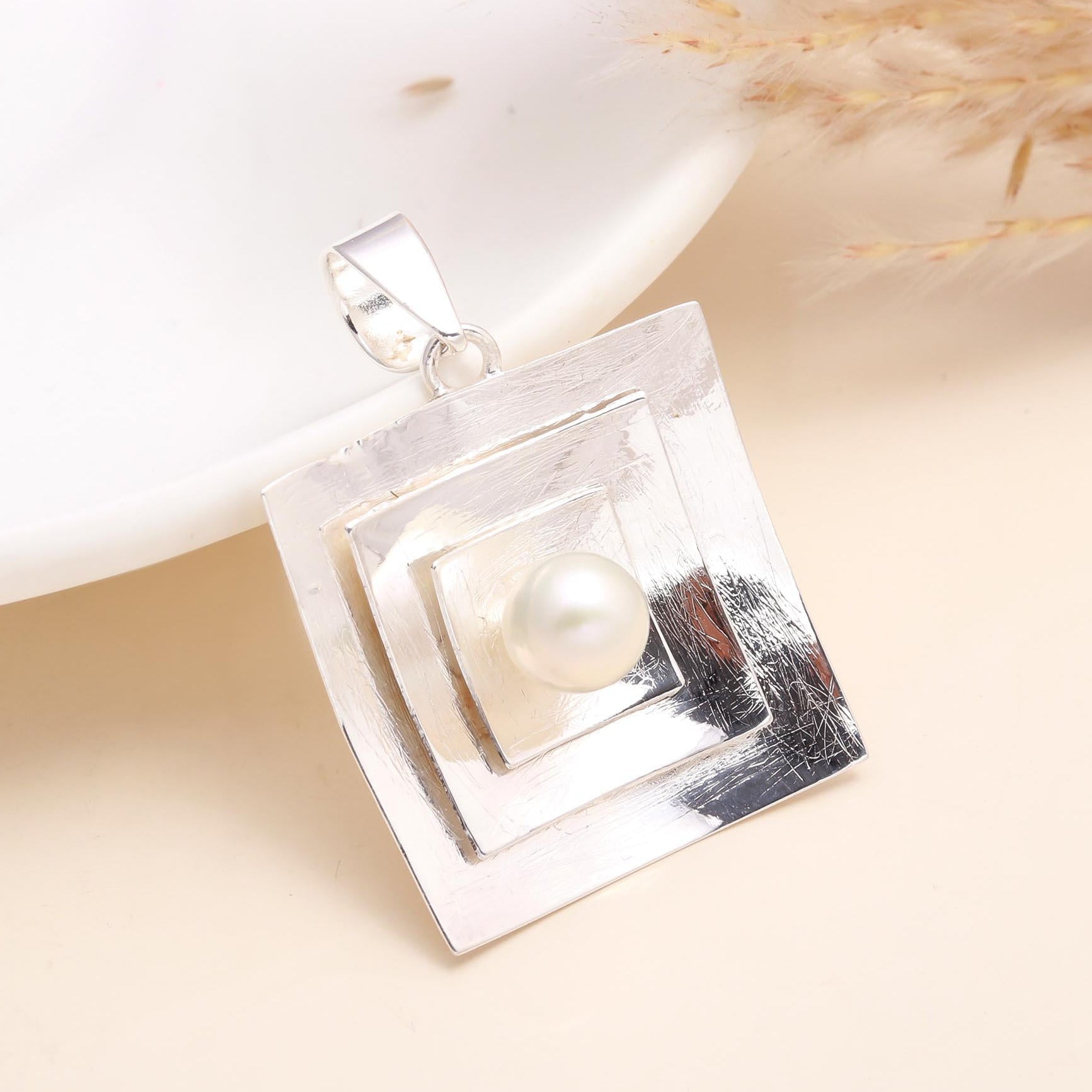Silver pendant with a pearl on a beige background