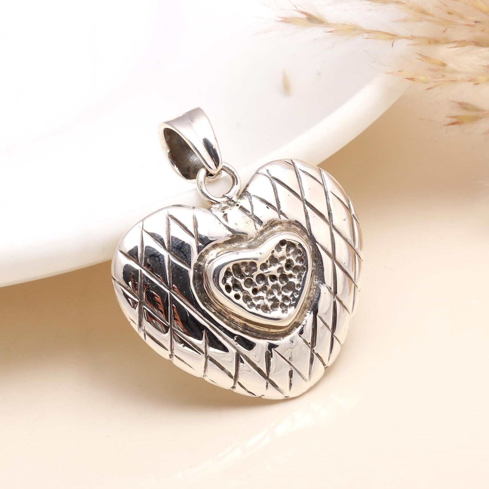A 925 sterling silver textured heart pendant displayed on a white surface, featuring a hammered finish with a heart pattern.