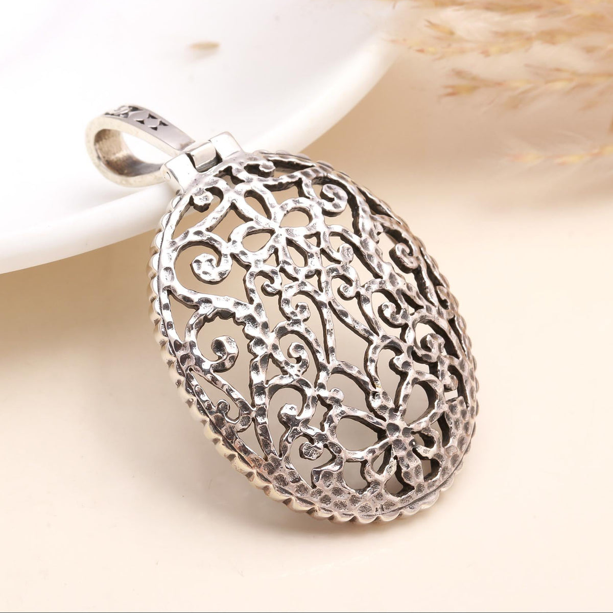 A sterling silver oval-shaped pendant with intricate filigree patterns, displayed against a neutral background.
