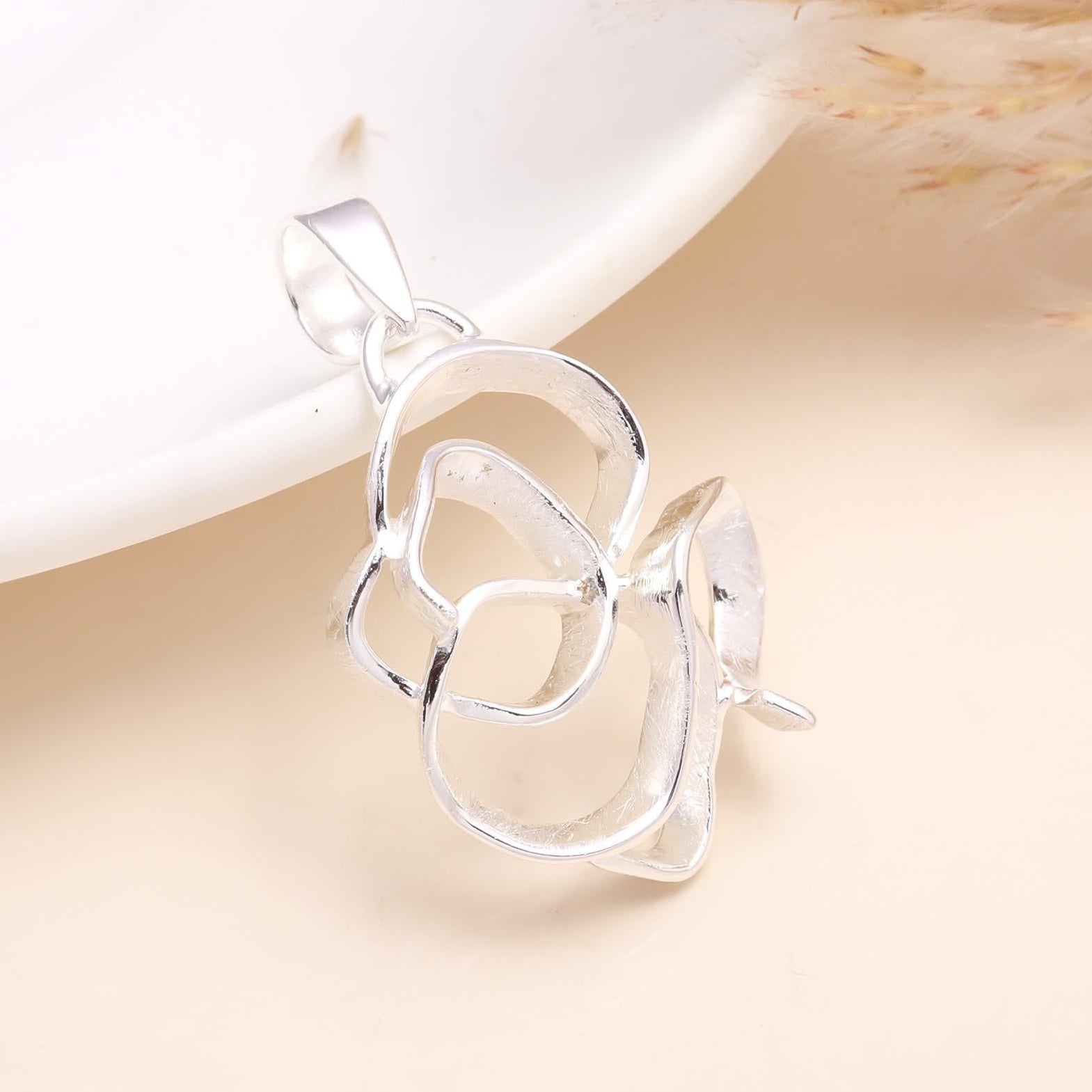 A 925 sterling silver abstract floral loop pendant on a white dish with a dry plant decoration to the side.