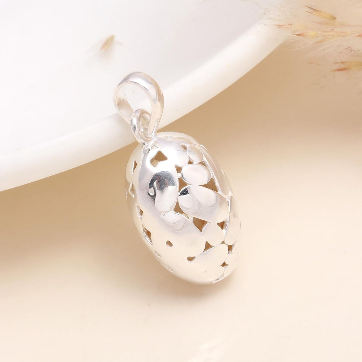 A 925 sterling silver hollow floral cutout oval pendant displayed against a light background, with natural light illuminating the intricate cutouts.