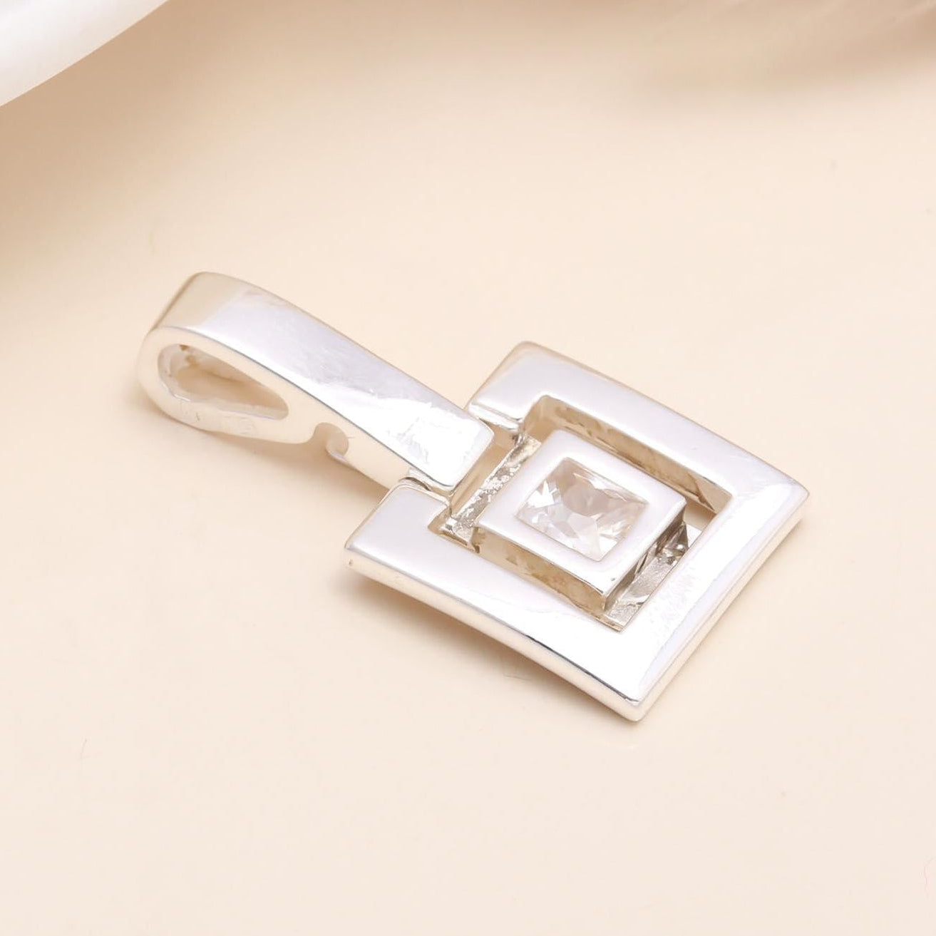 Silver pendant with a square design on a beige background