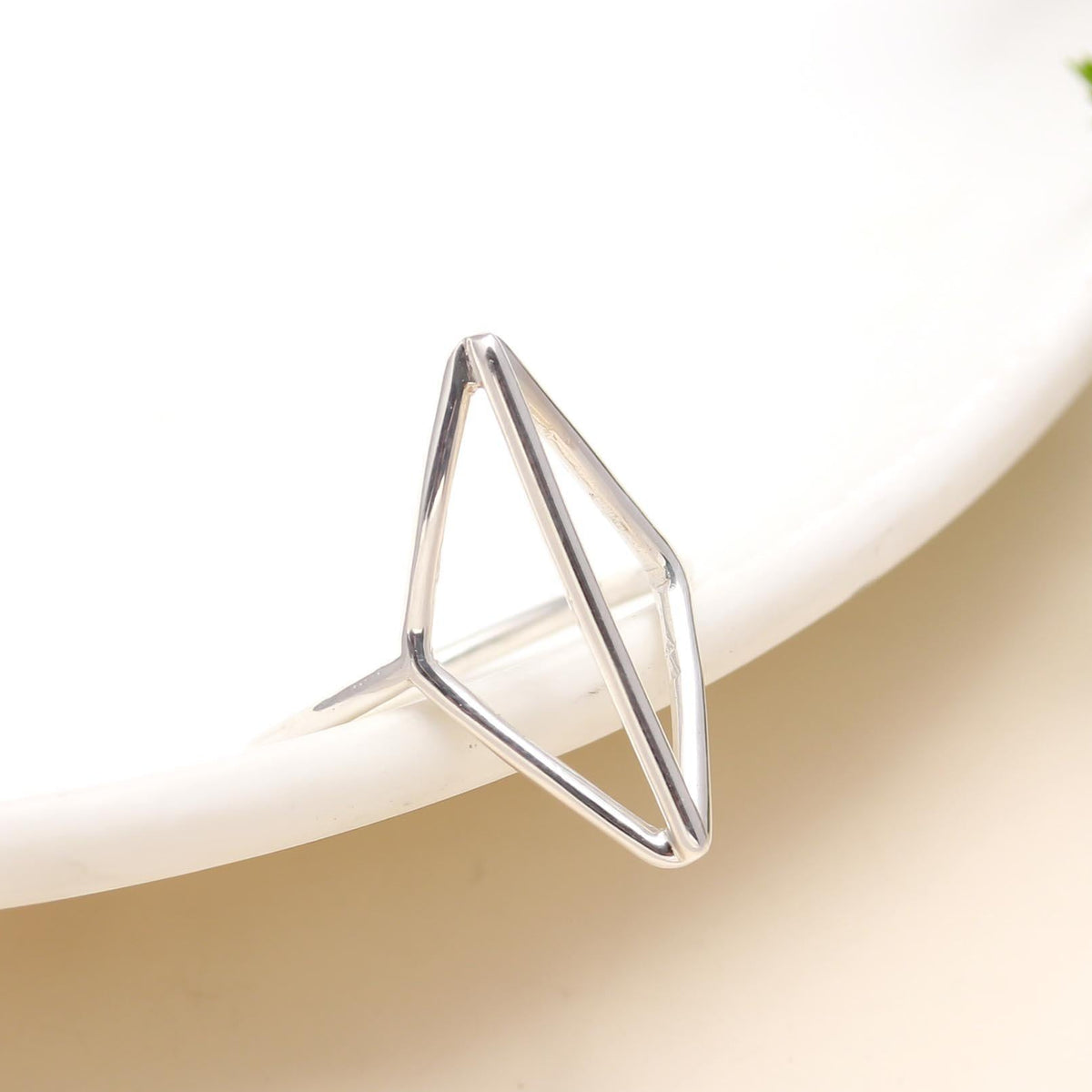 Silver geometric ring on a white and beige gradient background