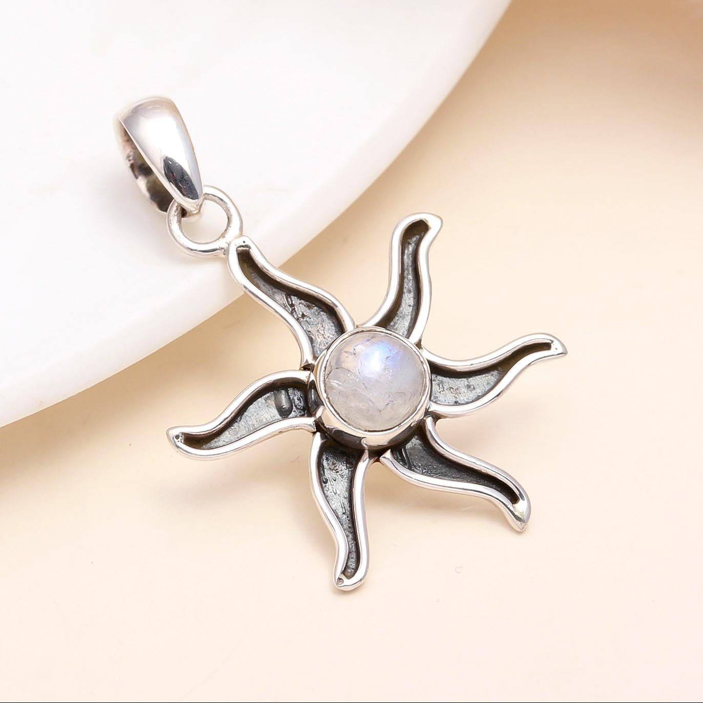 A silver sunburst pendant with a central moonstone, presented on a white dish.