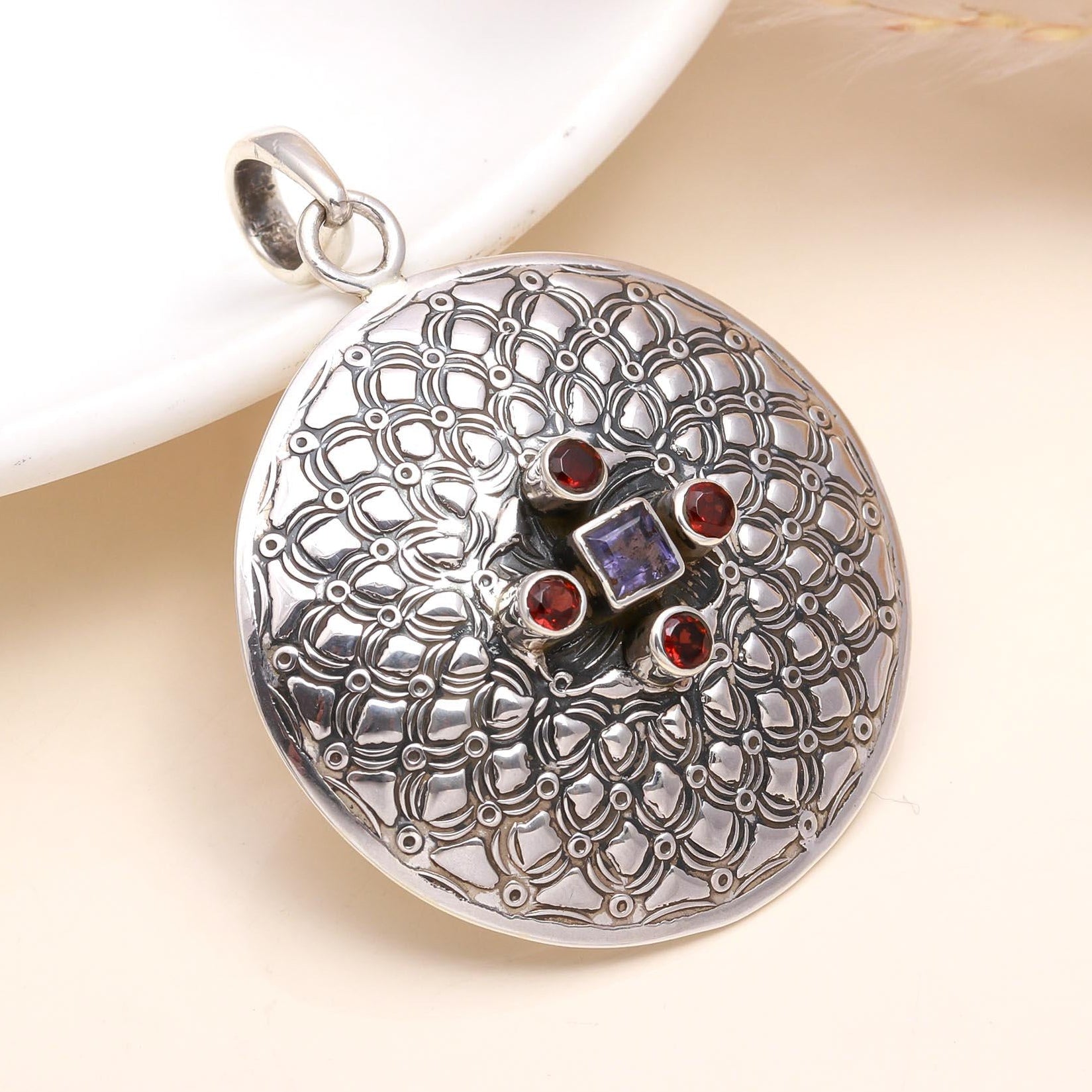 A round 925 sterling silver pendant with filigree design and inset with a deep red garnet and a violet-blue iolite.