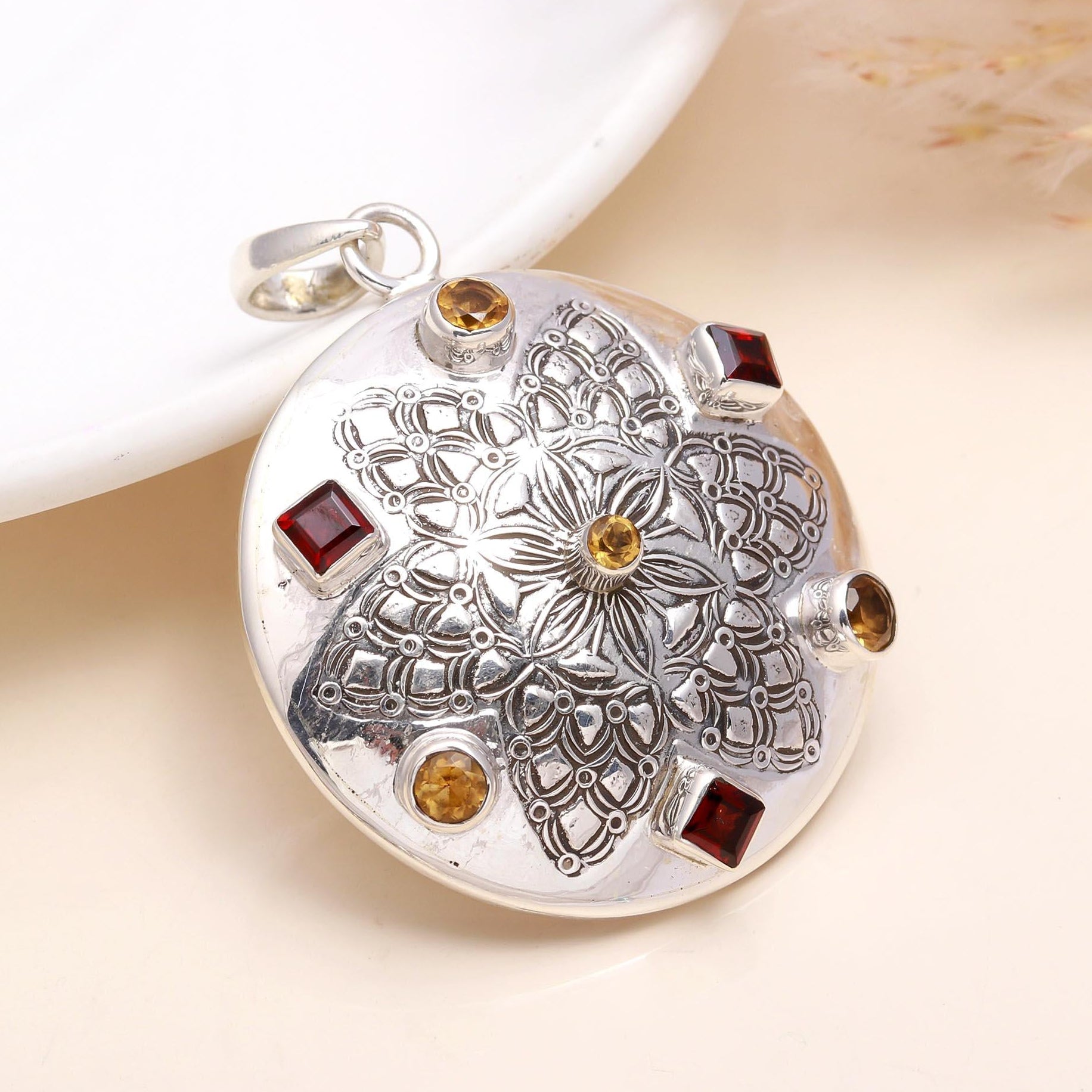 A sterling silver pendant featuring a garnet and citrine gemstone with intricate engravings on the silver surface.