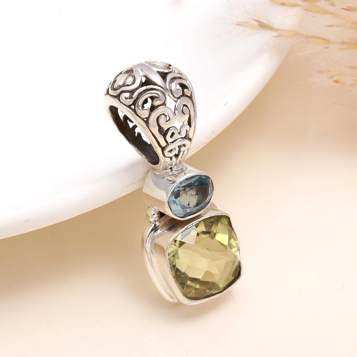 A sterling silver pendant featuring a blue topaz and a lemon quartz gemstone, presented on a white surface.