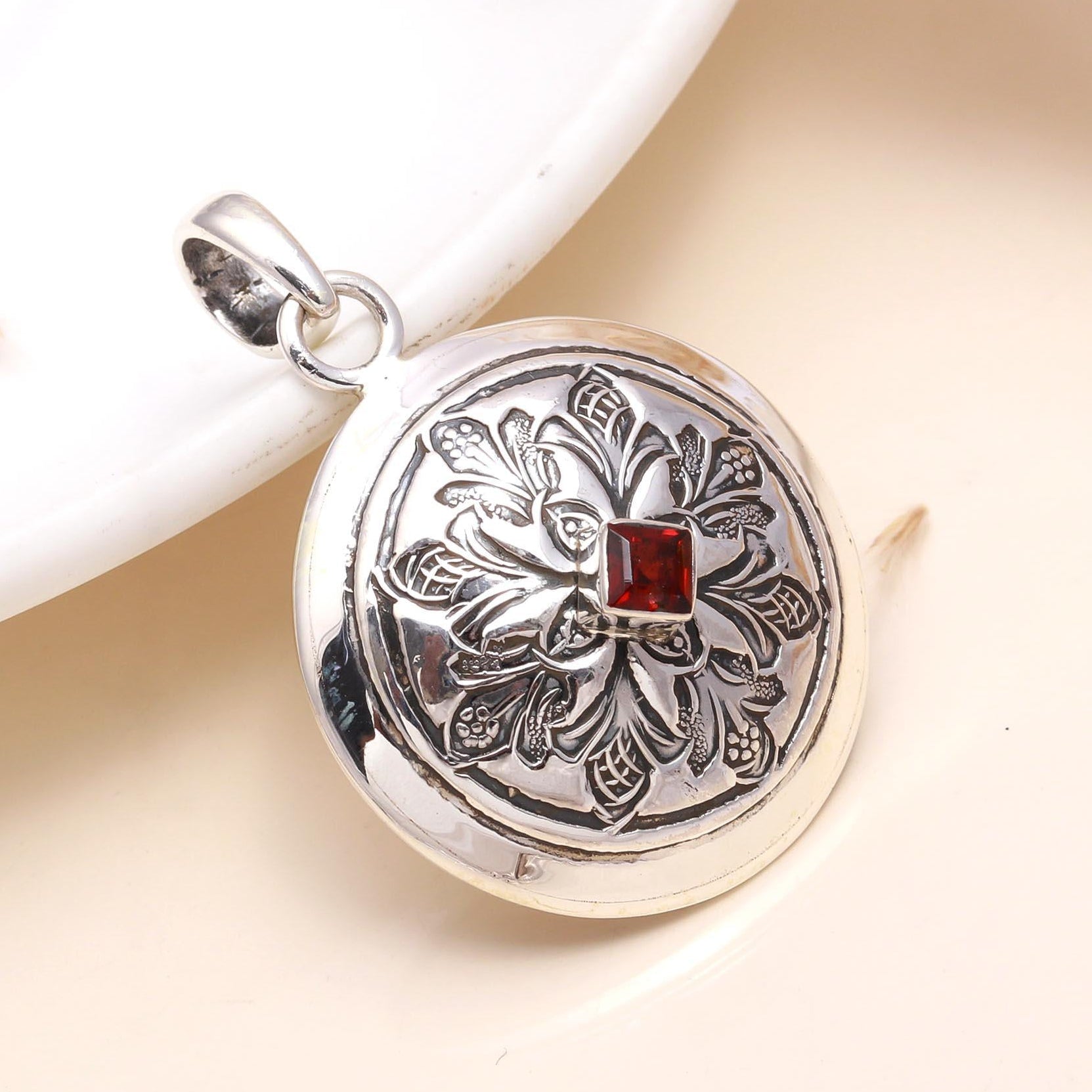 A vintage-style round sterling silver medallion pendant with a red garnet in the center, displayed against a white background.