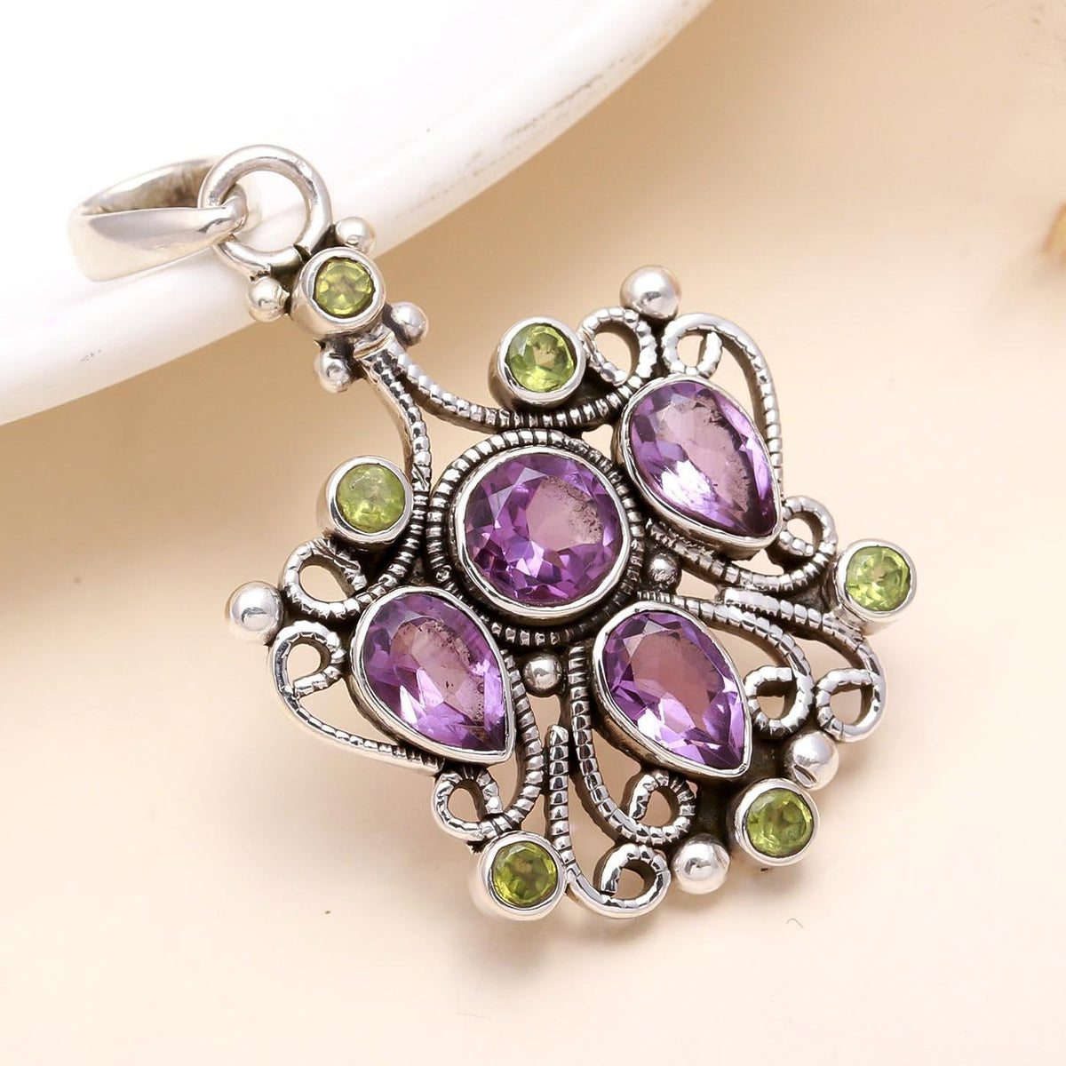 A sterling silver pendant featuring a vintage design with filigree work, adorned with deep purple amethyst and radiant green peridot gemstones.