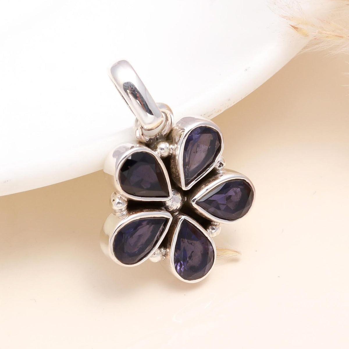 A sterling silver pendant with a flower design and a deep violet-blue natural iolite gemstone, displayed against a neutral background.