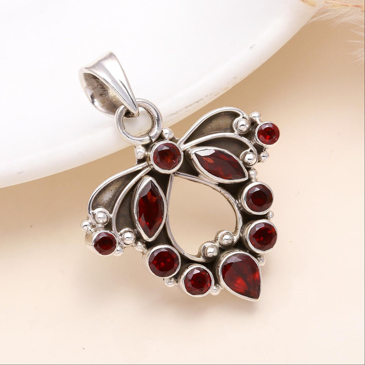 A sterling silver pendant with multiple red garnet stones set within a intricate, floral-like design against a neutral background.