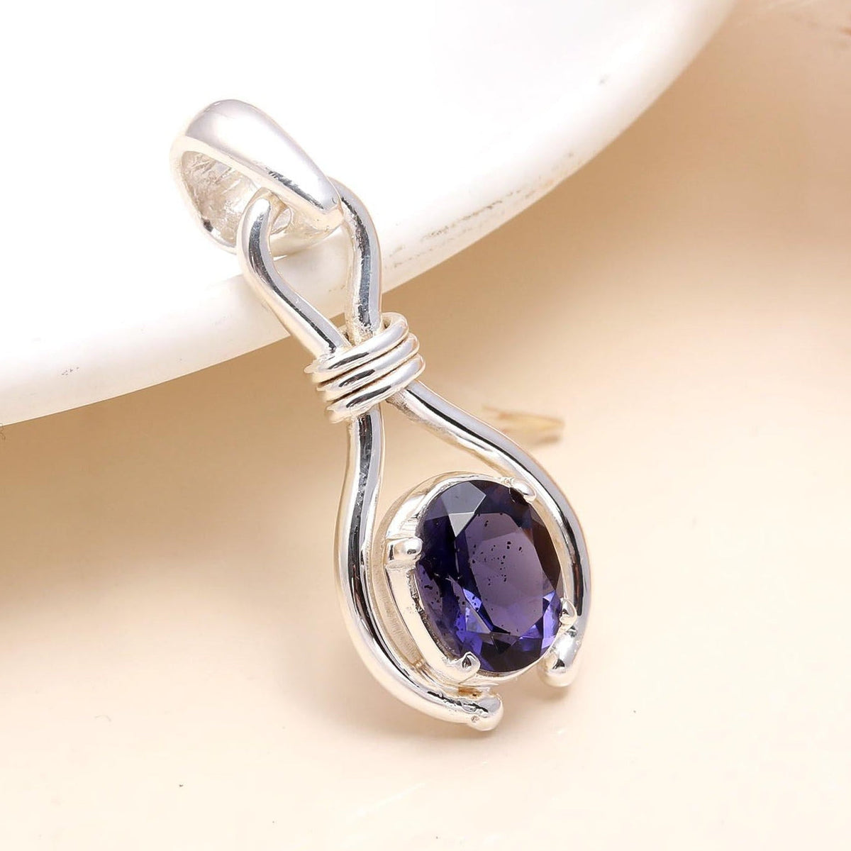A 925 Sterling Silver Blue Faceted Iolite Pendant placed on a white surface, highlighting the gemstone's facades and the silver mounting.