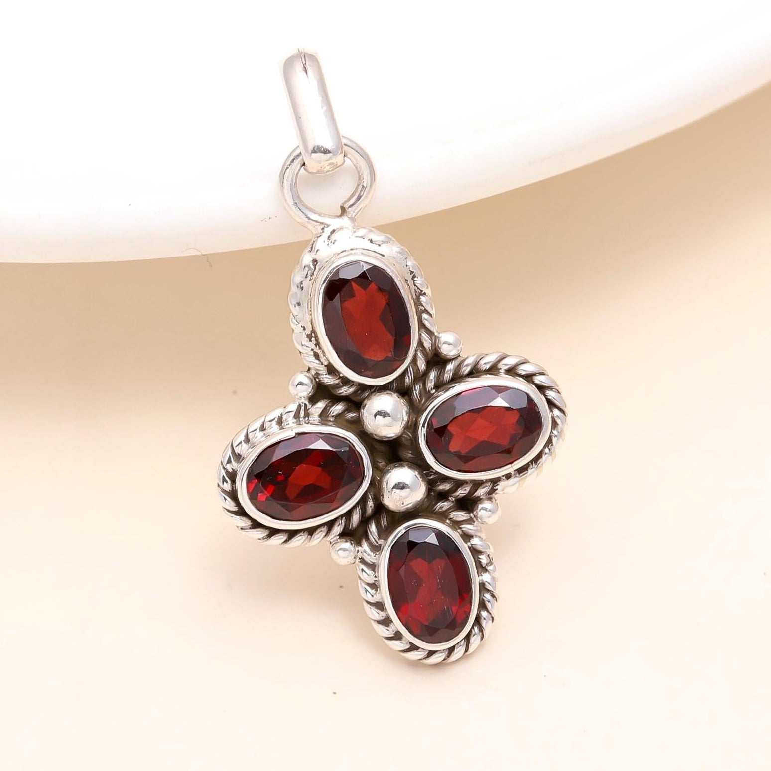 A sterling silver cross pendant with multiple garnet gemstones set within it, presented against a neutral background.
