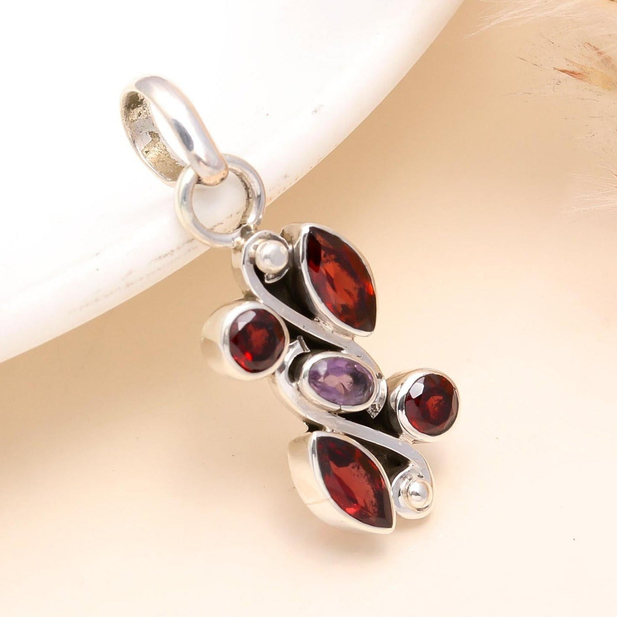 Silver pendant with red and purple gemstones on a light background