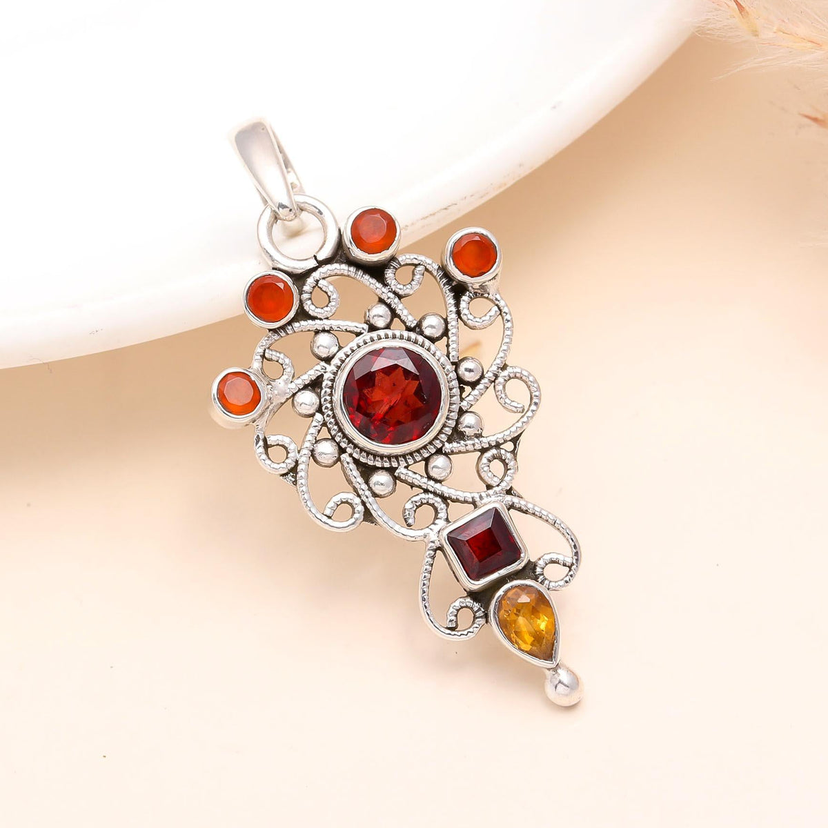 A sterling silver pendant featuring a vintage design with garnet and citrine gemstones, presented against a neutral background.