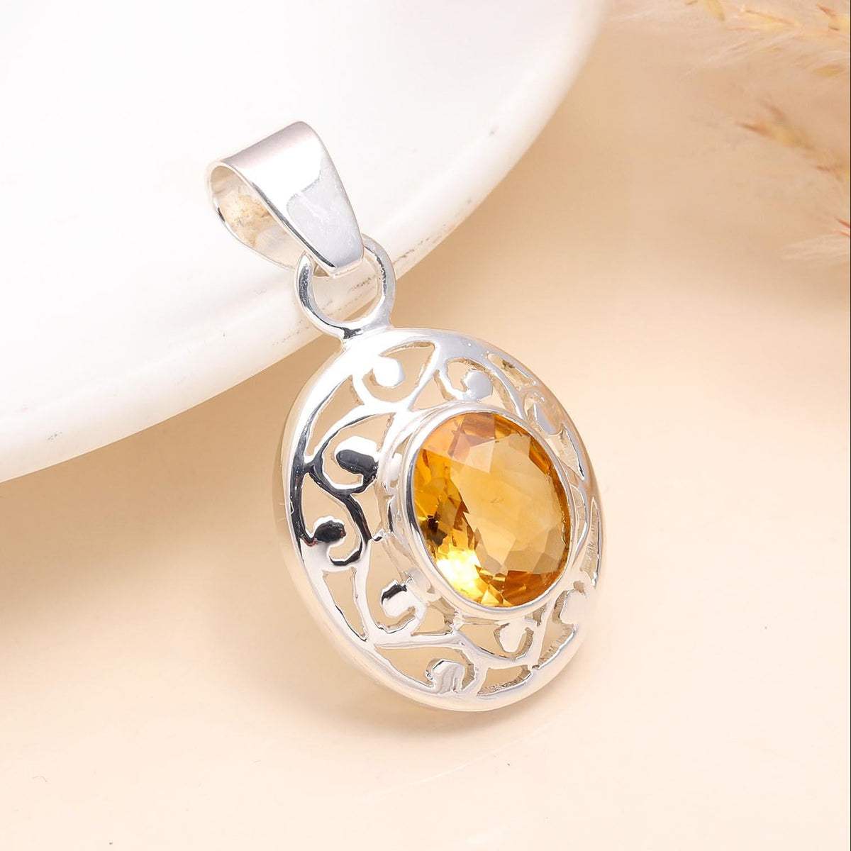 Silver pendant with a yellow gemstone on a beige background