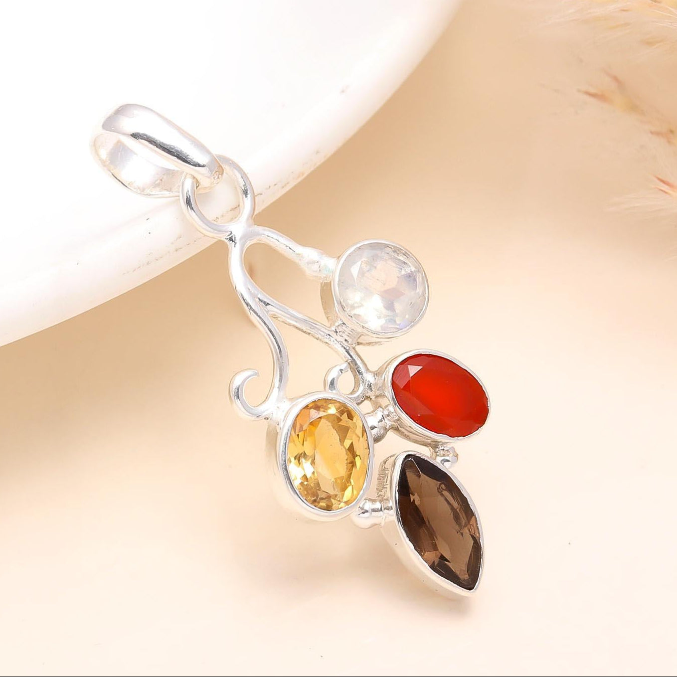 A silver pendant featuring a collection of multicolored gemstones including citrine, moonstone, carnelian, and smoky quartz, set against a neutral background.
