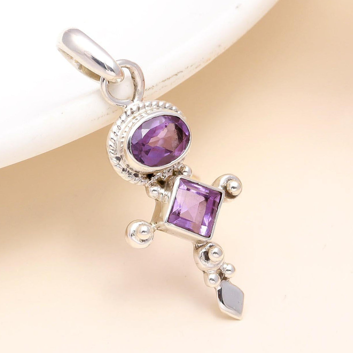 Silver pendant with purple gemstones on a beige background