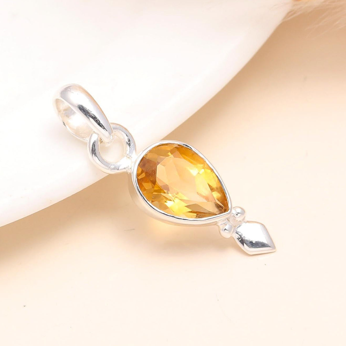 A pear-shaped citrine gemstone set in a sterling silver teardrop pendant mount, placed against a neutral background.