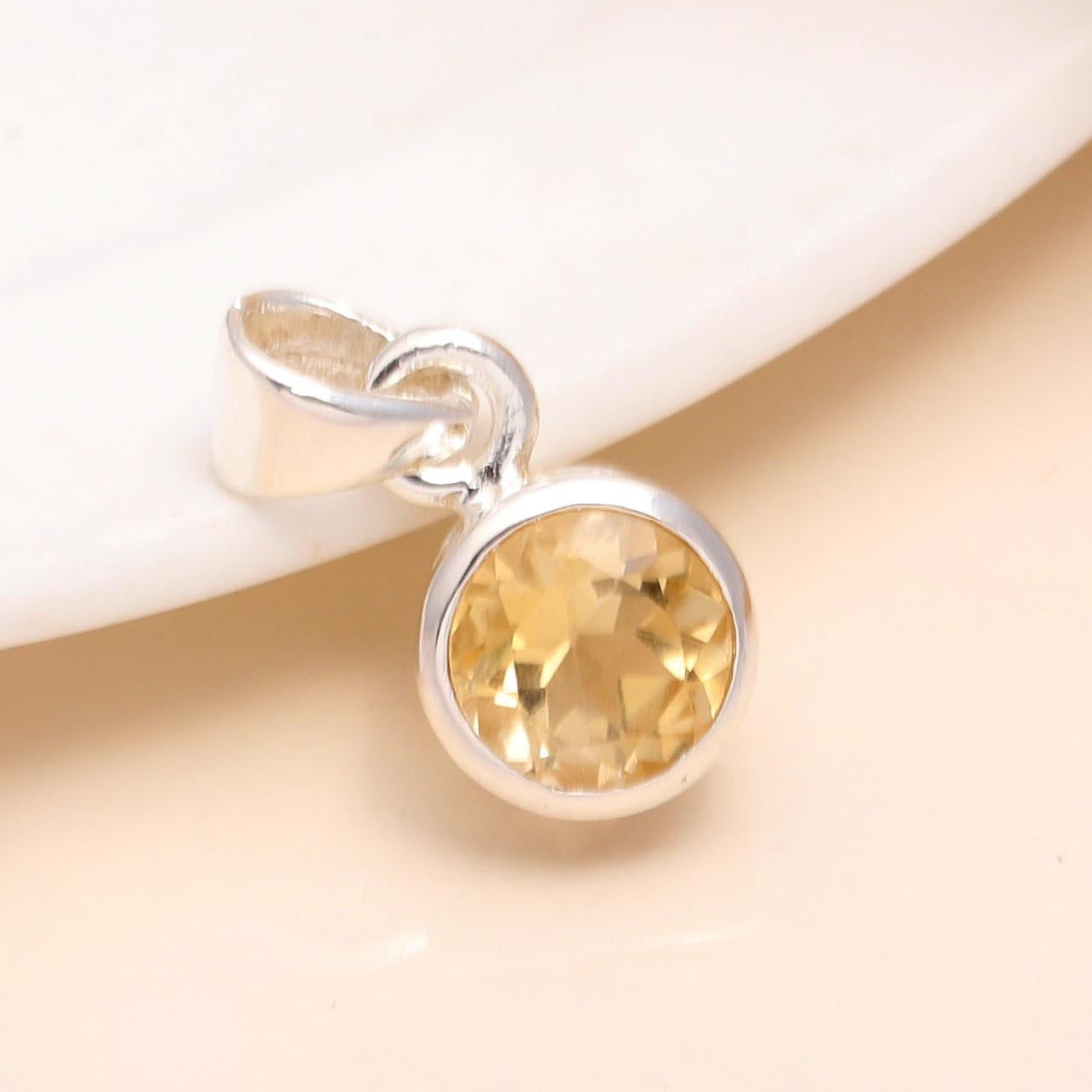 A 925 Sterling Silver Round Citrine Classic Minimalist Pendant placed on a white surface with a hint of foliage at the top edge.