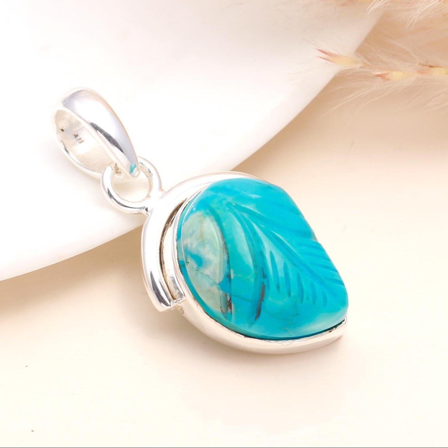 A hand-carved turquoise pendant set in sterling silver, displayed against a neutral background.