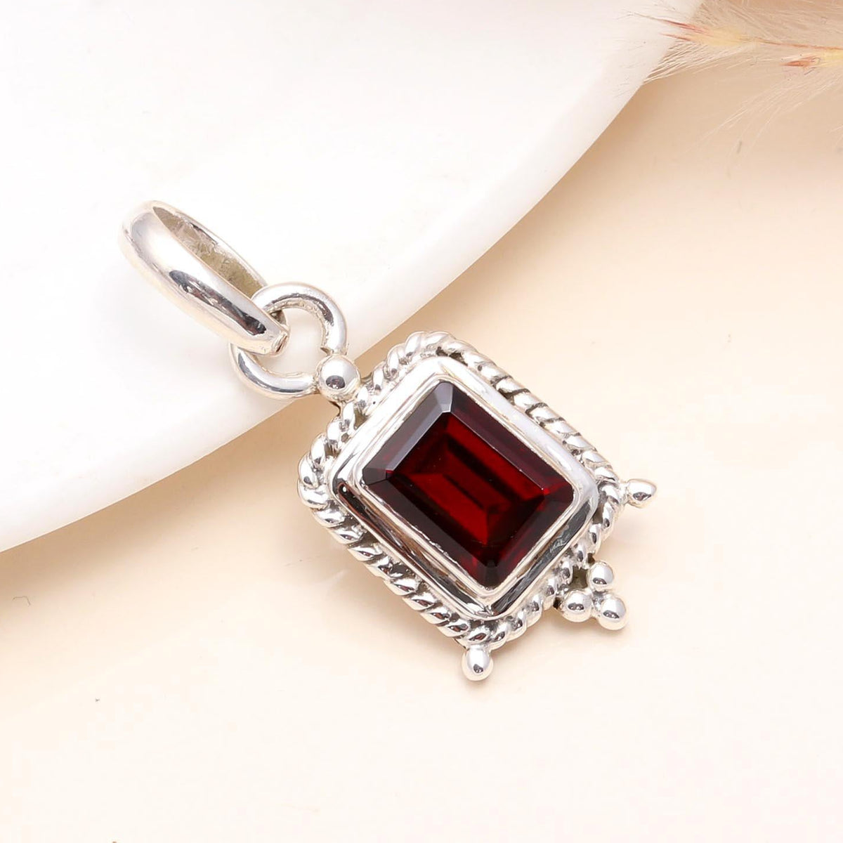 A sterling silver vintage-inspired square garnet pendant with intricate detailing, presented against a neutral background.