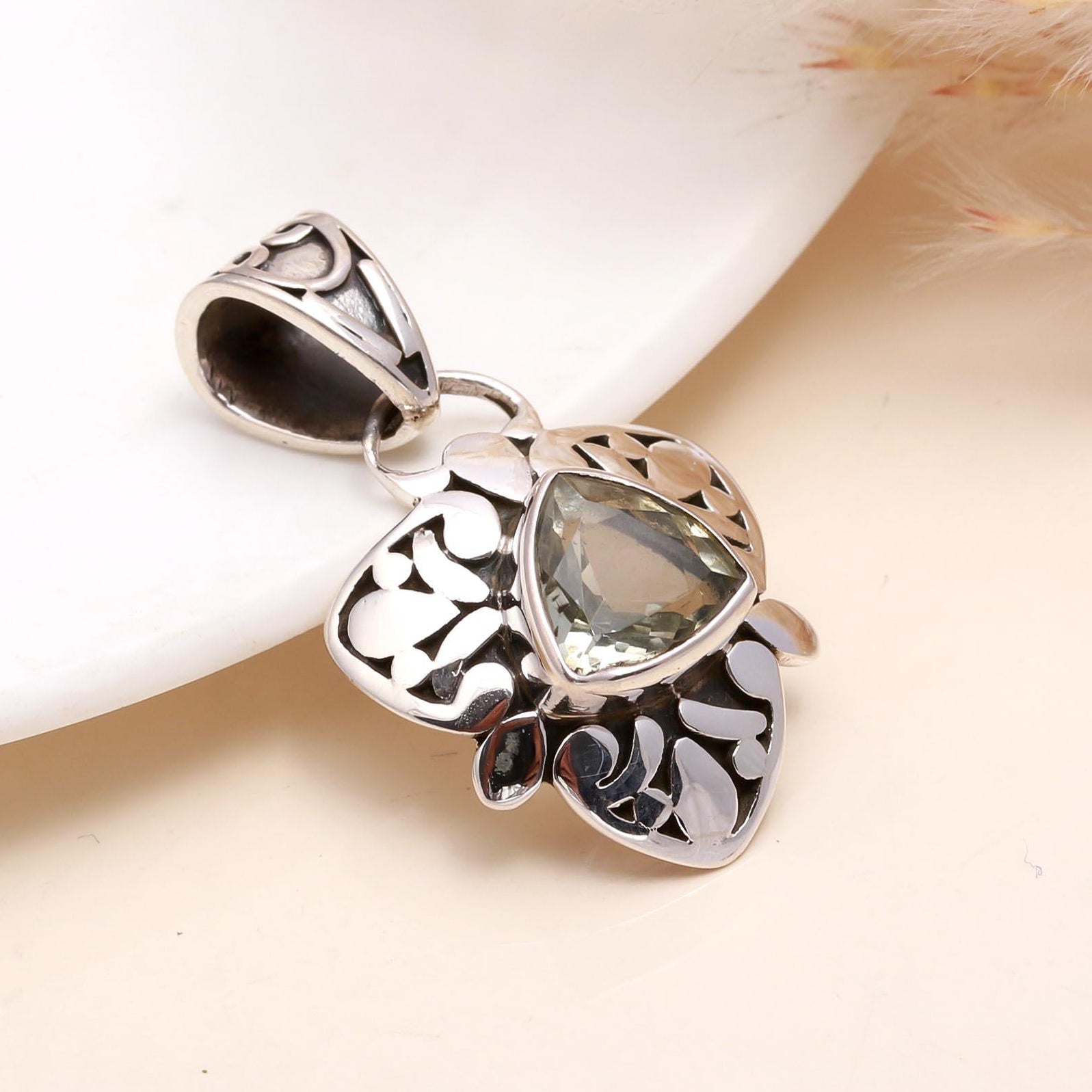 A trillion-cut green amethyst gemstone pendant with intricate filigree silverwork, displayed against a neutral background.