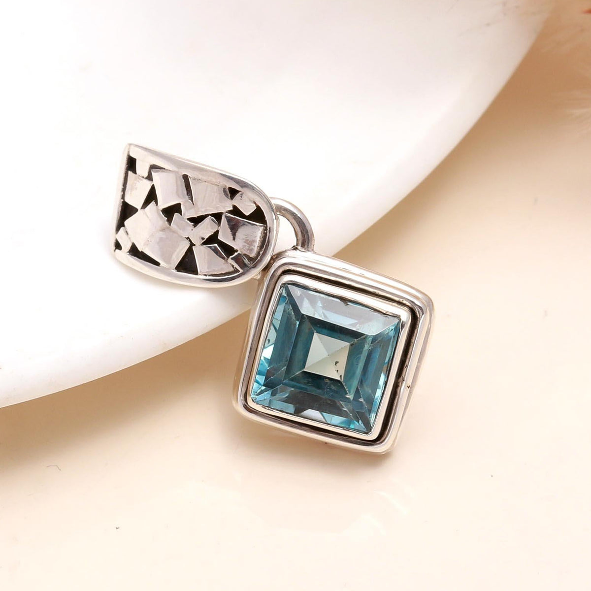 A square-cut blue topaz pendant set in a sterling silver geometric square setting, displayed against a neutral background.