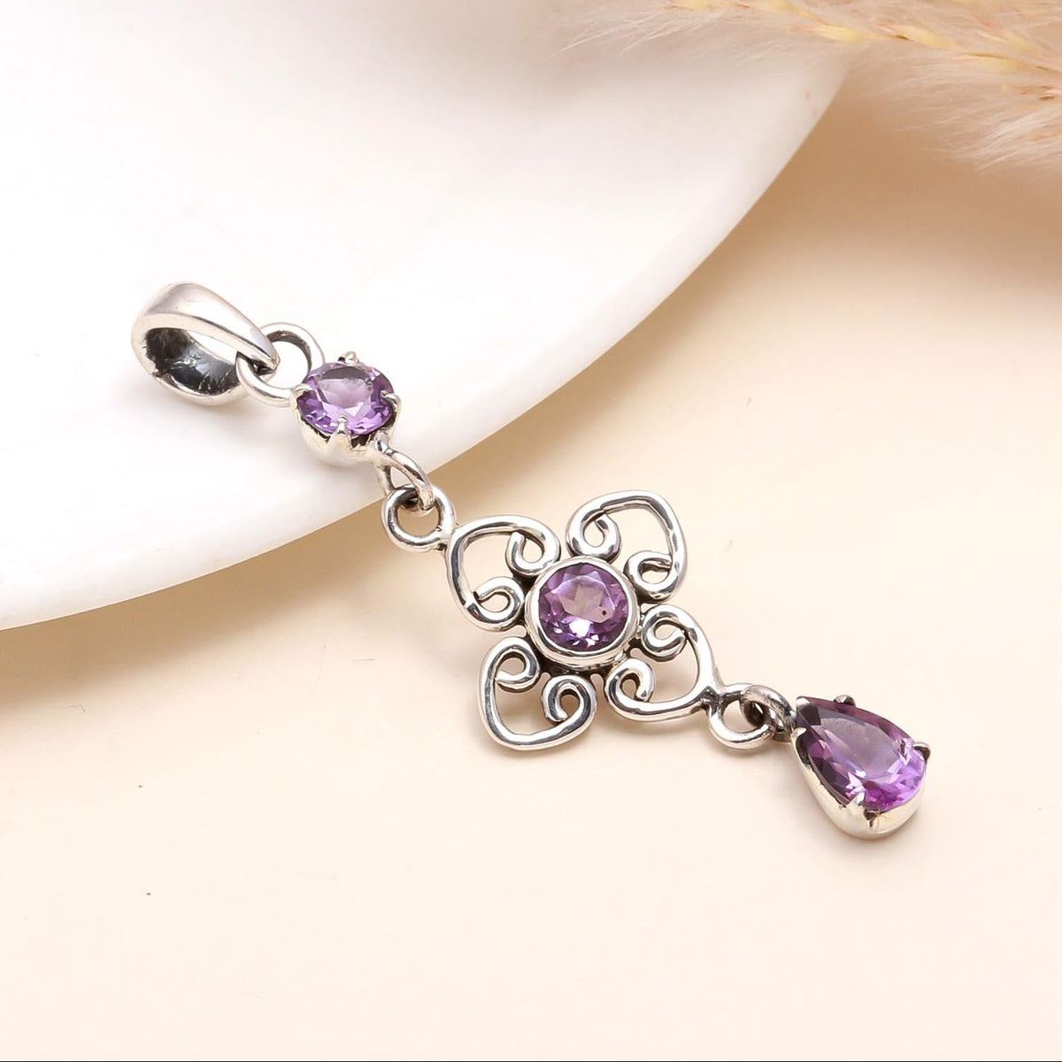 A sterling silver pendant with a deep purple amethyst gemstone and intricate filigree detailing, presented on a white surface.