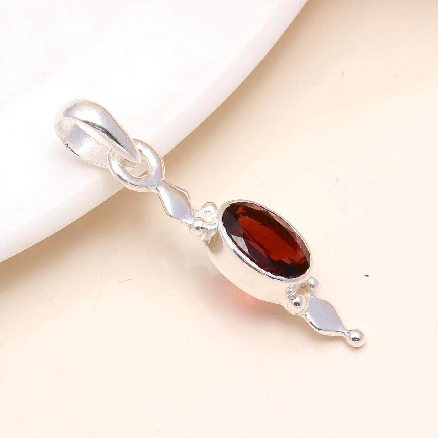 Silver pendant with a red gemstone on a beige background