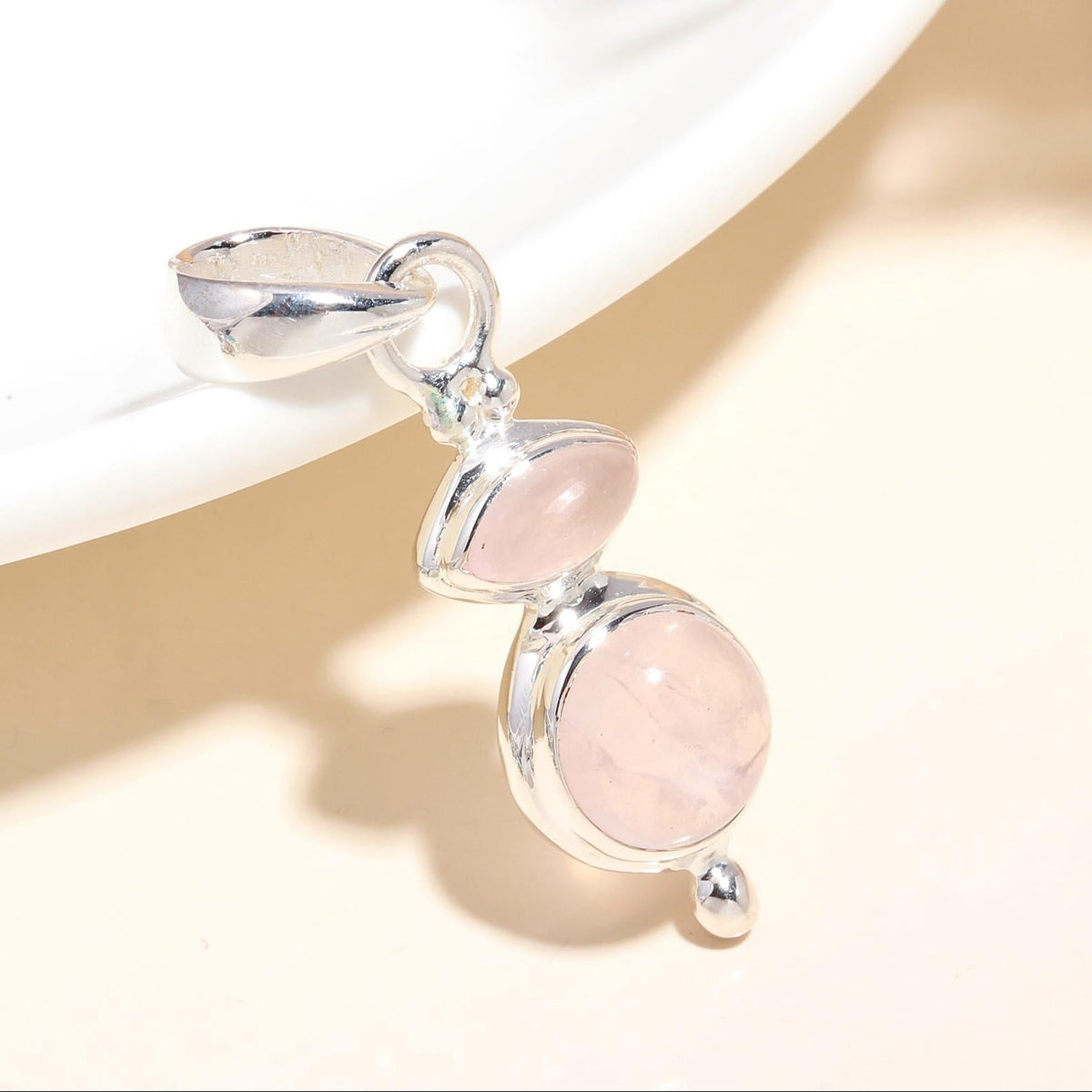 A silver pendant with two rose quartz gemstones, presented on a white surface with a shadow cast upon it.