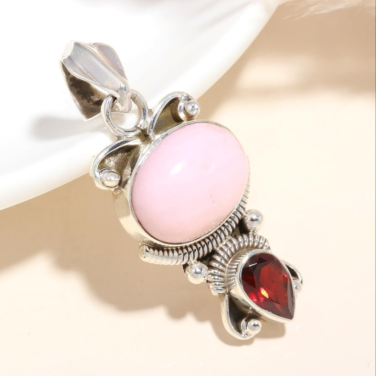 A vintage-style sterling silver pendant featuring a pink rose quartz main stone and a deep red garnet, with intricate silver filigree detailing.