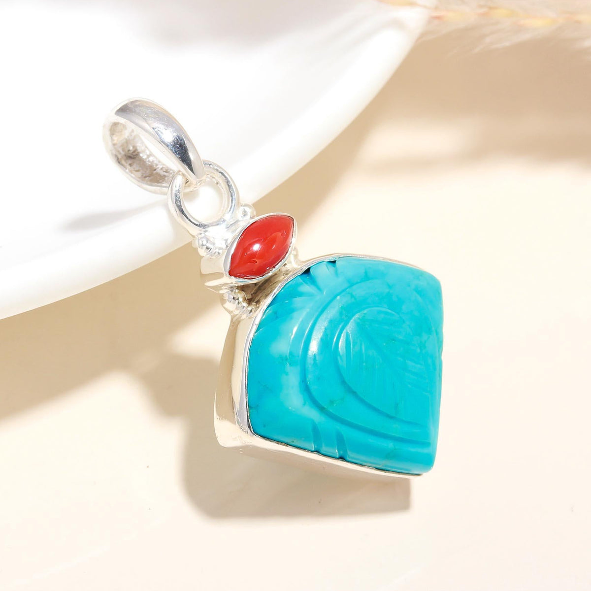 A sterling silver pendant featuring hand-carved natural turquoise and coral, displayed against a neutral background.