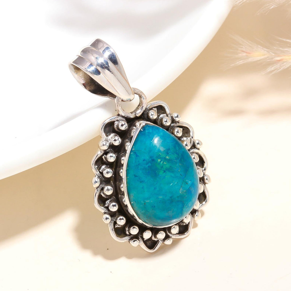 A teardrop-shaped natural turquoise gemstone pendant, set in a sterling silver mounting with intricate filigree details, displayed against a neutral background.