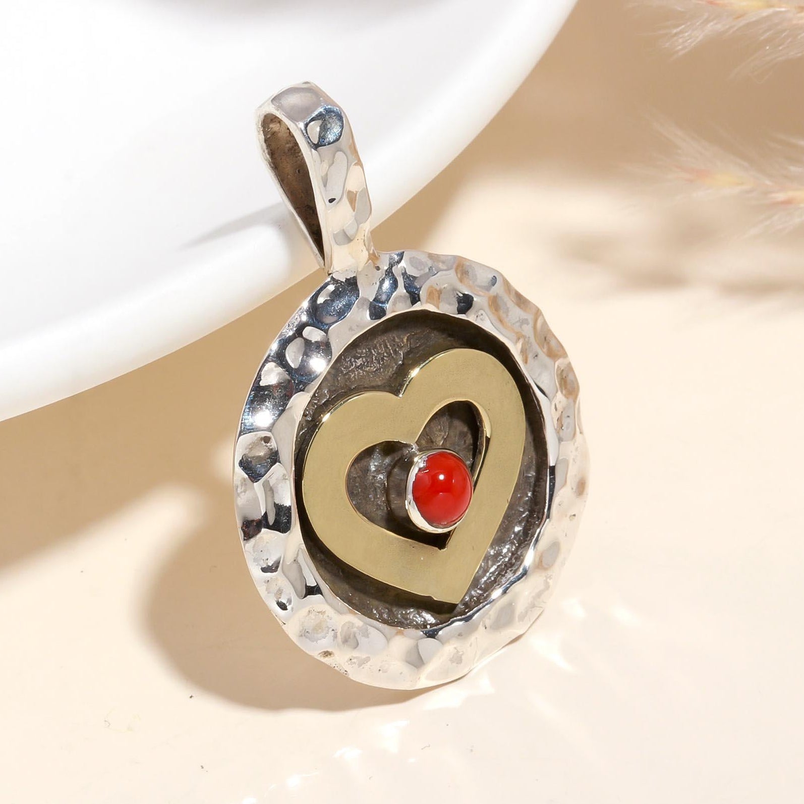 A heart-shaped sterling silver pendant with a hammered texture and a red coral inset at the center, displayed against a neutral background.