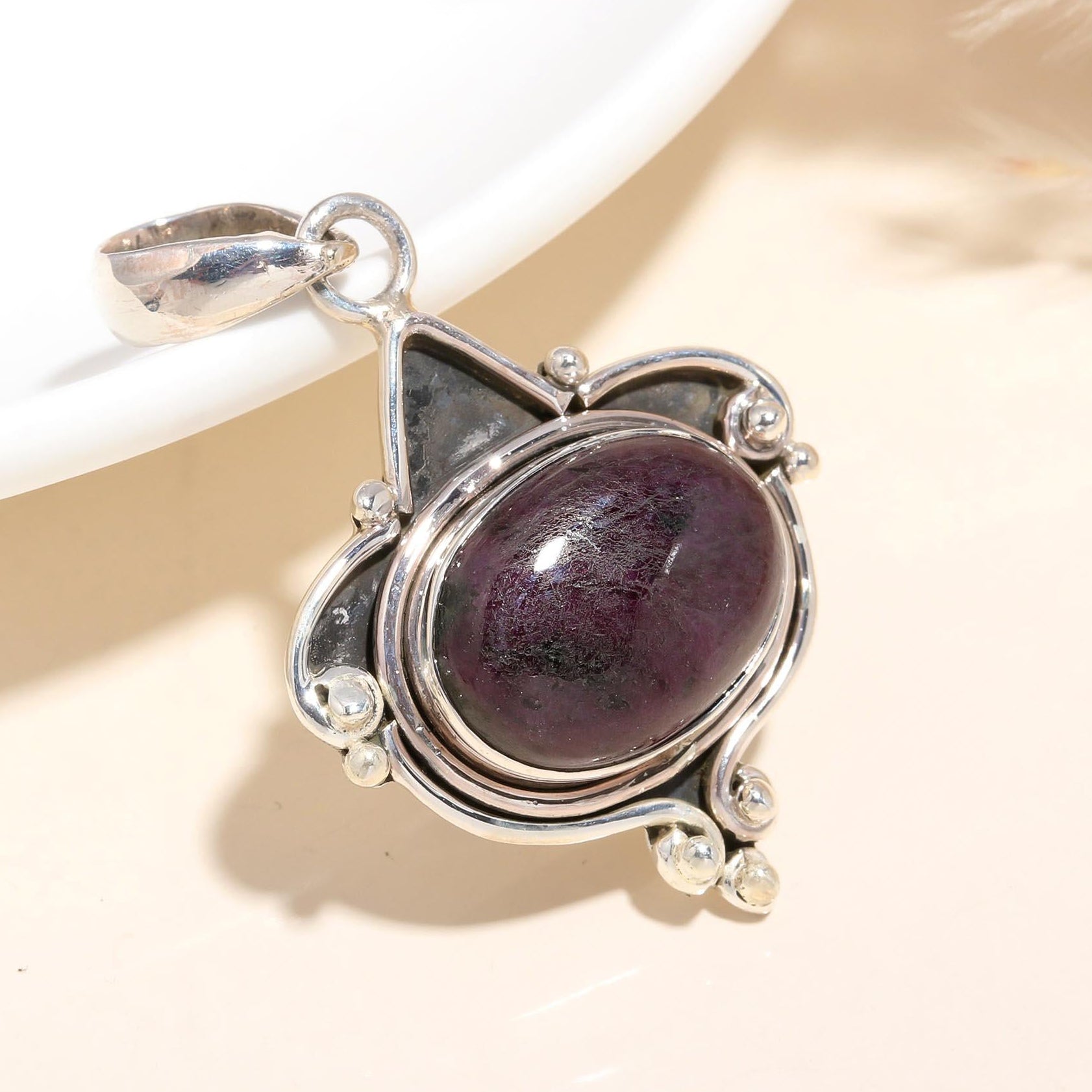 A sterling silver pendant featuring an oval-cut ruby zoisite with vintage-inspired design.